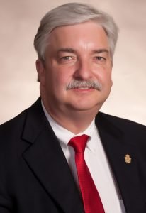 Dr. Frank Buck, productivity expert and author, in a professional headshot wearing a black suit and red tie.